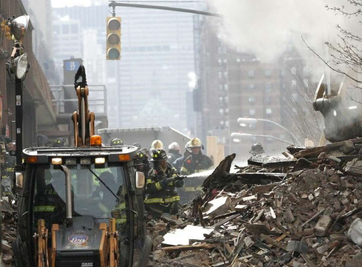 A firefighter applies water to rubble a day after a gas leak-triggered explosion, Thursday, March 13, 2014, in East Harlem, New York. Rescuers working amid gusty winds, cold temperatures and billowing smoke pulled additional bodies Thursday from the rubble of two apartment buildings that collapsed Wednesday.
