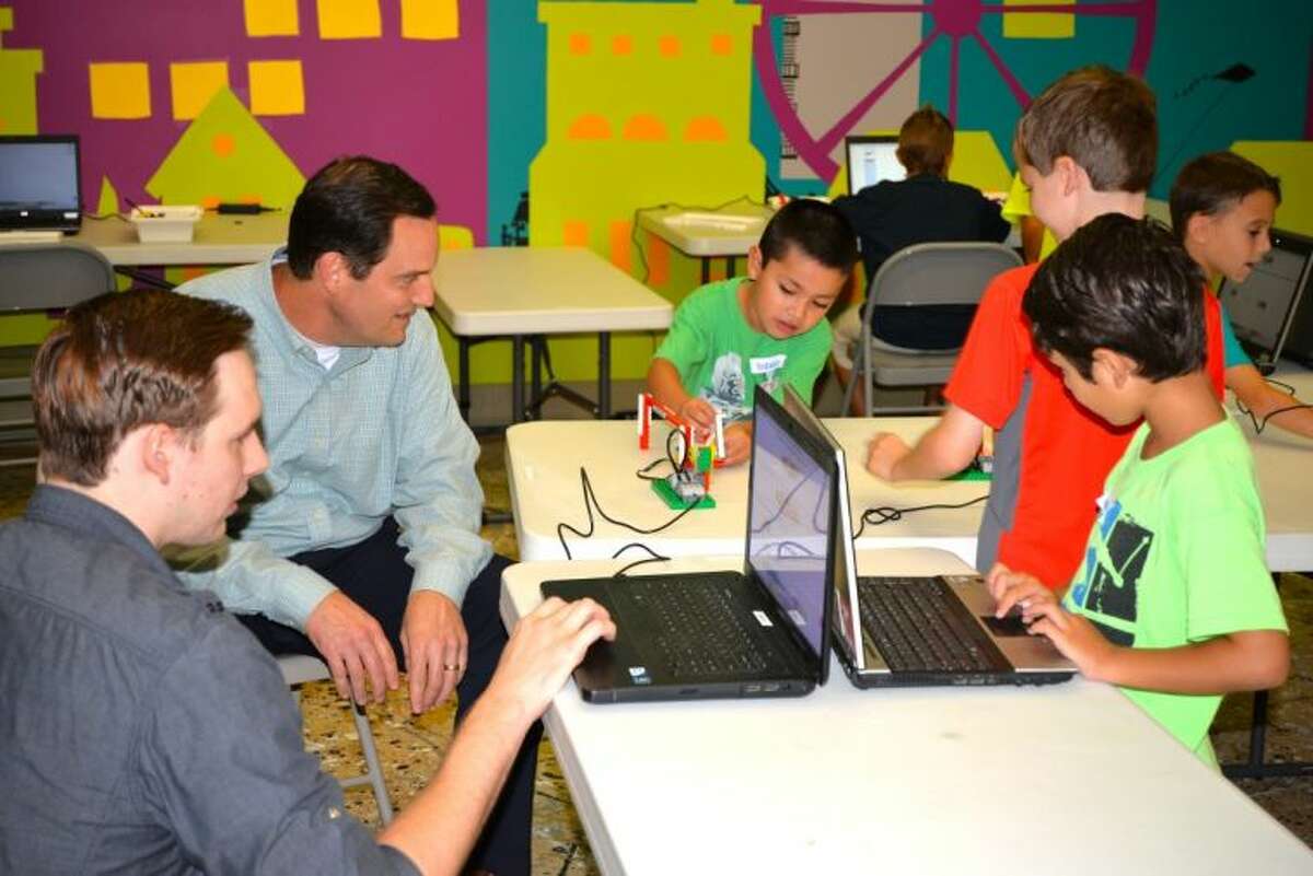 Mike Rohm (top left), manager of IT administration for Anadarko Petroleum Corporation, visits with students and their teacher, Jeremy Lukk (bottom left) in the Lego Robotiks class at The Woodlands Children’s Museum. The donated computers made it possible for the class to take advantage of new software and take their robots to the next level.