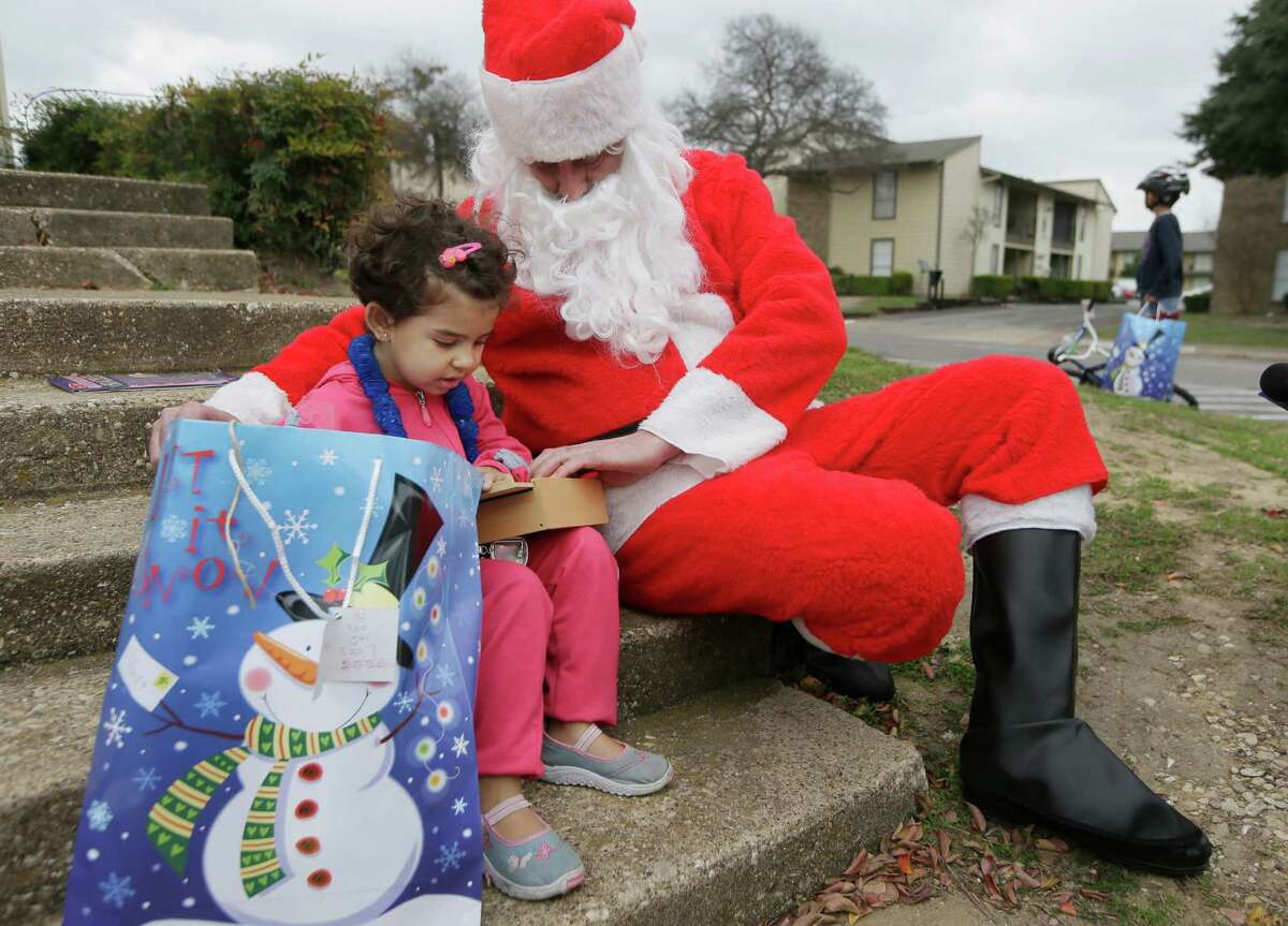 Newly arrived Syrian refugee Jory, 4, left, receives a gift outside her family's apartment from volunteer Tim Blystone, right, portraying Santa Claus Dec. 12, 2015, in Dallas.