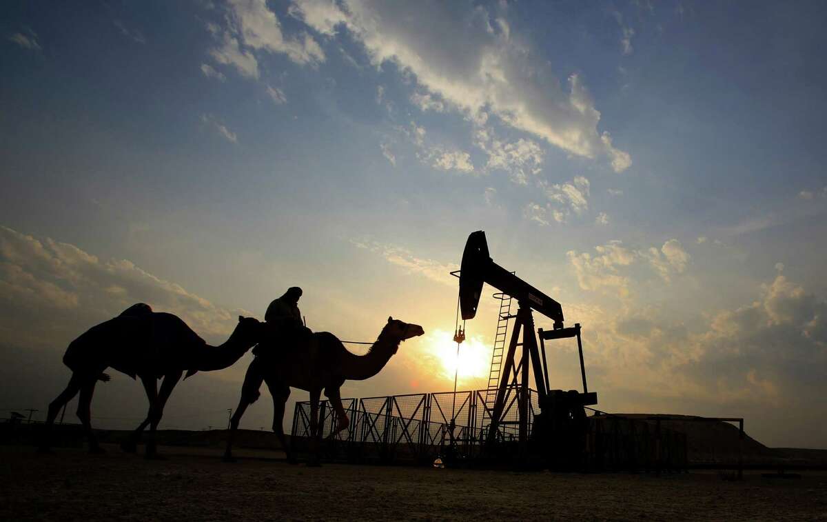 A man rides a camel through the desert oil field.