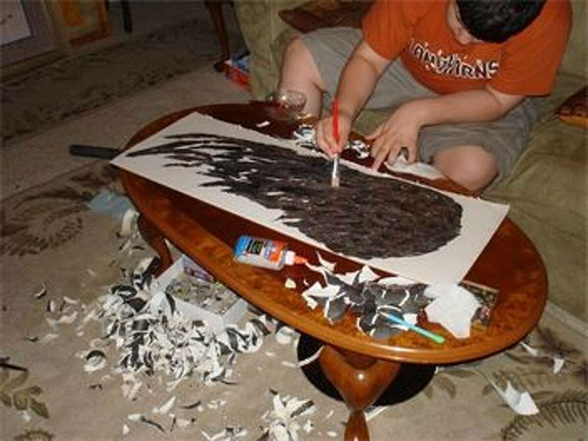 Award-winning eco-artist Grant Manier at work in his home with mounds of shredded paper on the floor. Not wanting to get glue on his hands, he uses a paintbrush to apply the clear glue on his masterpieces.