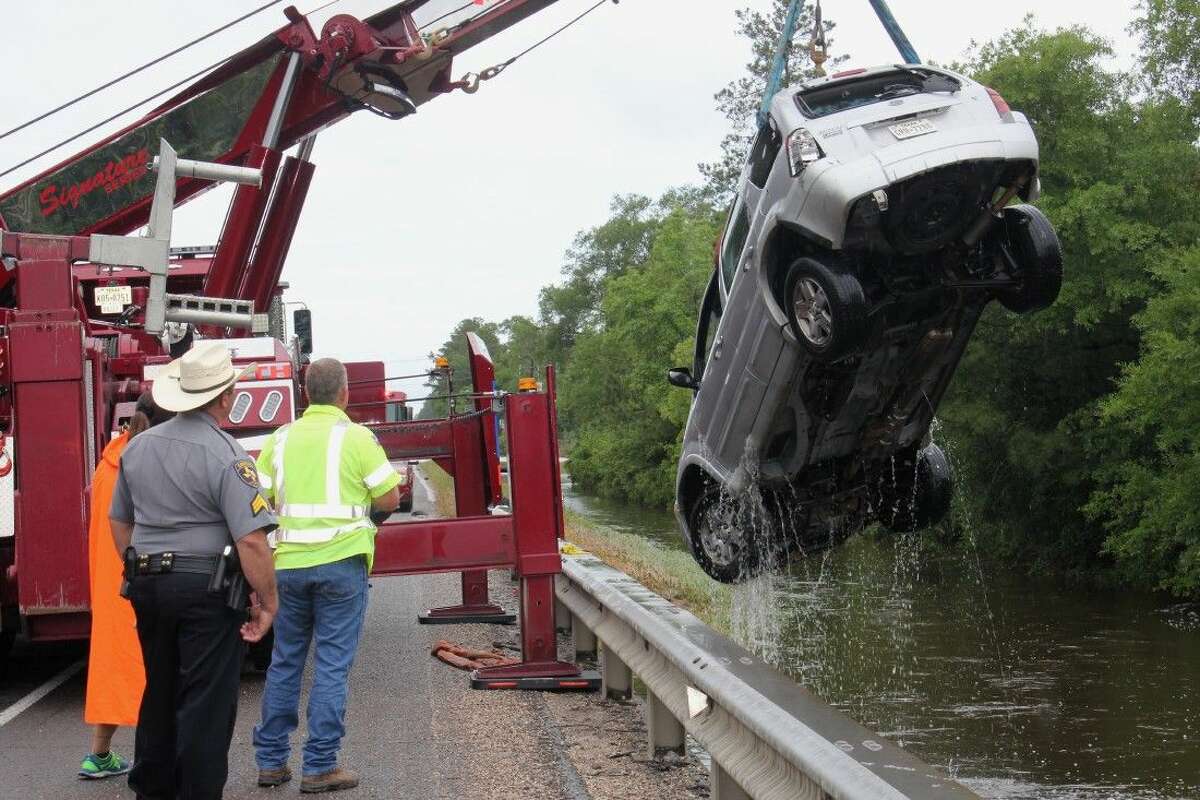 A tow truck owned by Smith Towing of Cleveland lifts a flooded vehicle from Tarkington Bayou on Wednesday. The Ford Escape drifted into floodwaters on Monday, prompting the driver to be rescued by Cleveland Fire Department. Controlling the tow truck is Jesse Burch of Smith Towing while Pct. 5 Deputy Constable David Hunter and Linda Burch, also of Smith Towing, look on.