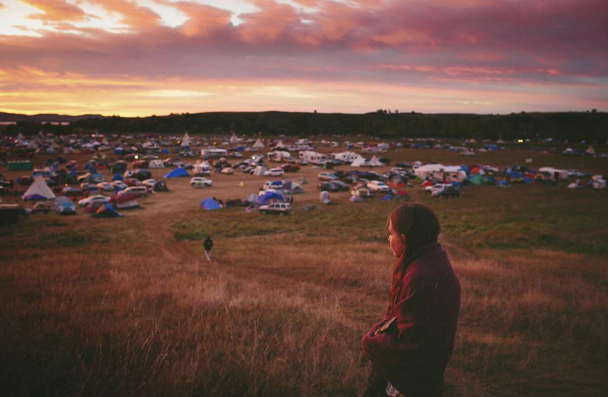 Susan Leopold of the Patawomeck Tribe of Virginia, watches the sun rise over the Sacred Stone Camp, where thousands of Native Americans have joined the Standing Rock Sioux tribe�s protest against an oil pipeline, in Cannon Ball, N.D., Sept. 9, 2016. Ranchers and residents in the conservative, overwhelmingly white countryside view the demonstrations with a mix of frustration and fear, reflecting the deep cultural divides and racial attitudes. (Alyssa Schukar/The New York Times)