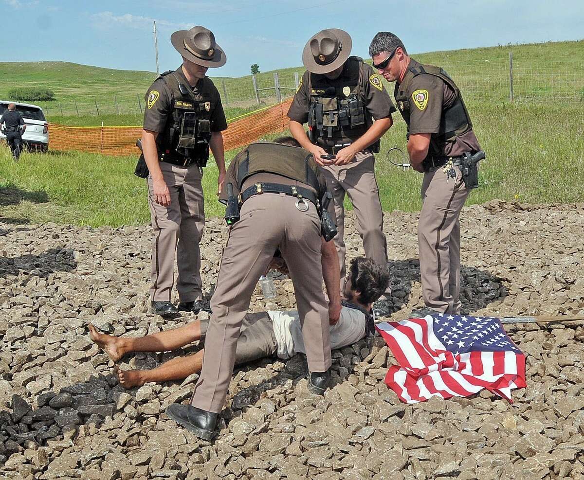 Law enforcement officers stand over a protester at the site of where a roadway was being built for construction of the Dakota Access Pipeline on Thursday, Aug. 11, 2016, in rural Morton County, N.D. The pipeline would start in North Dakota and pass through South Dakota and Iowa before ending in Illinois. (Tom Stromme/The Bismarck Tribune via AP)