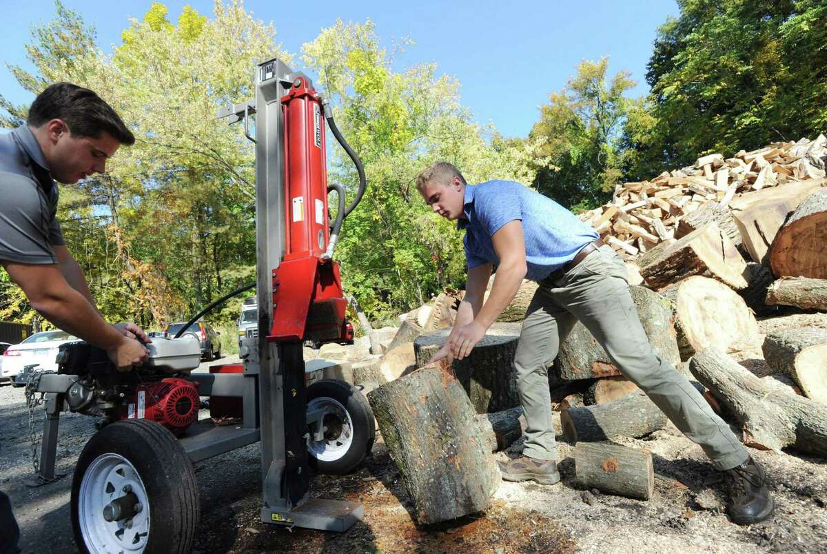 Brett Atkinson, left, works with his brother Scott Atkinson, right, as the pair use a machine to split wood on Tuesday.