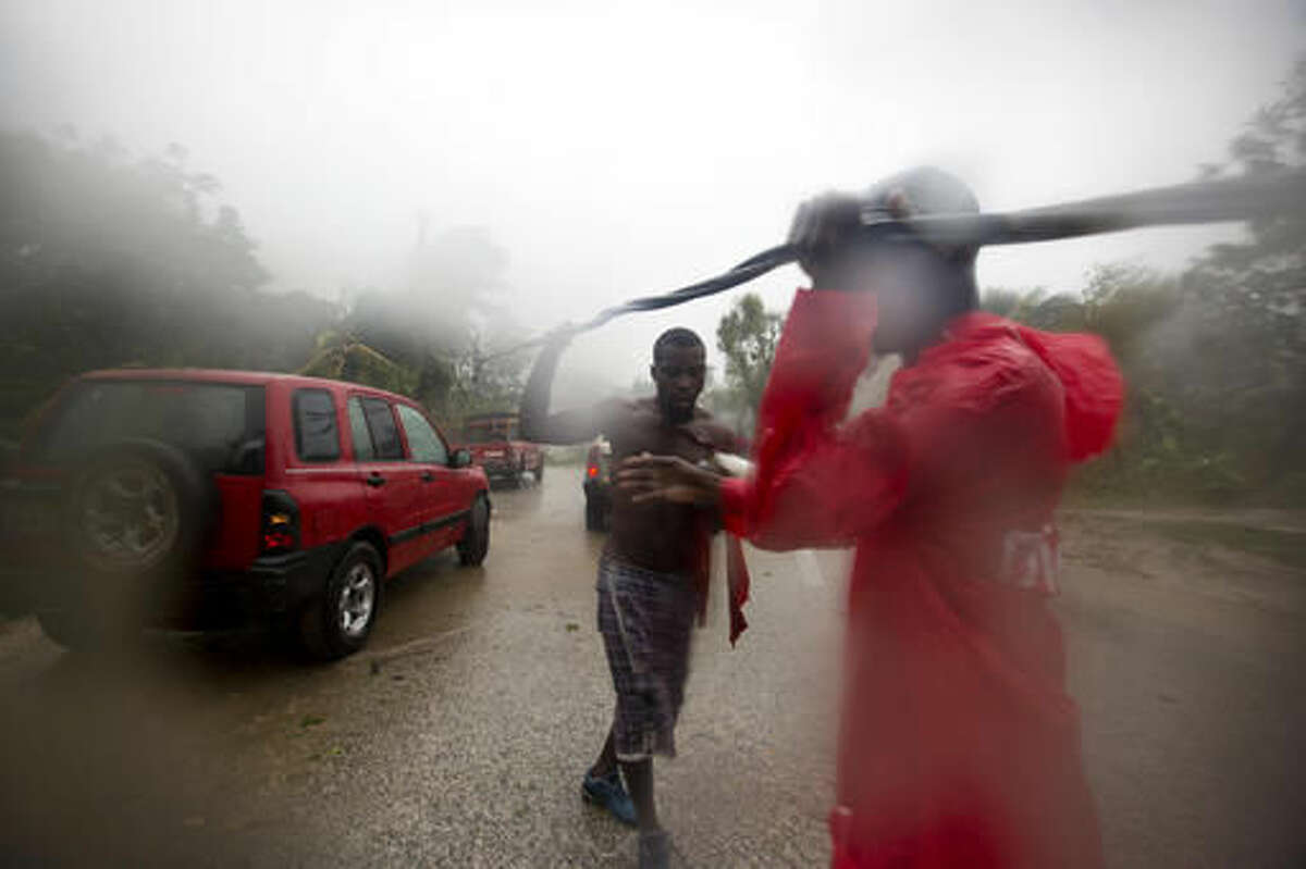 Two men remove a downed power line to allow vehicles passage, in Petit Goave, Haiti, Tuesday, Oct. 4, 2016. Matthew slammed into Haiti's southwestern tip with howling, 145 mph winds Tuesday, tearing off roofs in the poor and largely rural area, uprooting trees and leaving rivers bloated and choked with debris. ( AP Photo/Dieu Nalio Chery)