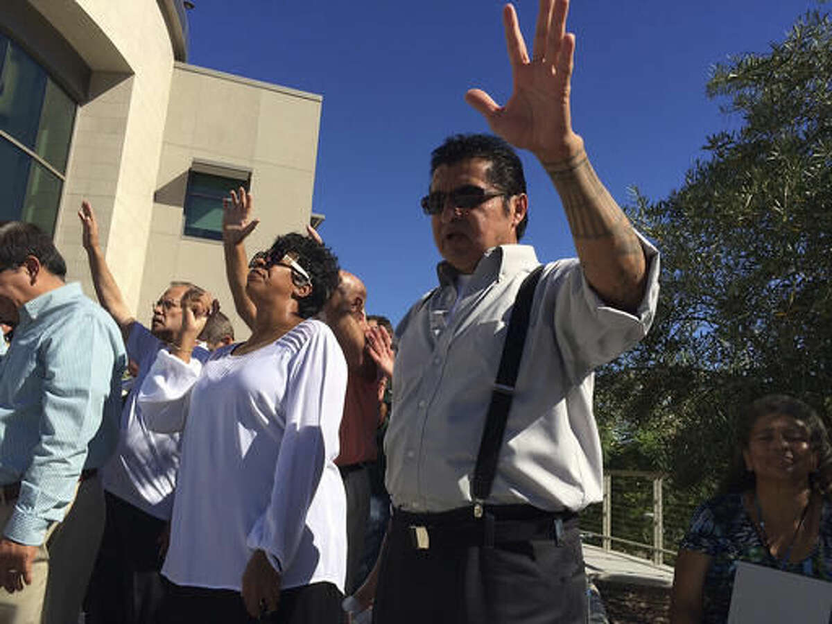 Pastor Richard Cisco Mendez, right, joins members of the community praying outside El Cajon Police Department station in El Cajon, Calif., on Friday, Sept. 30, 2016. Ministers led dozens of people in a prayer for unity, healing and peace Friday in a San Diego suburb following days of angry and sometimes violent protests over the police killing of an unarmed black man. The prayer service comes ahead of what's expected to be a large protest Saturday by the family of Alfred Olango and demonstrators upset over his killing and demanding the release of a video showing the incident. (AP Photo/Julie Watson)