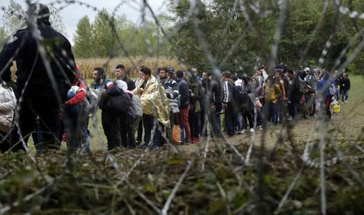FILE - In this Saturday, Sept. 26, 2015 file photo, a group of migrants, seen through razor wire, crosses a border from Croatia near the village of Zakany, Hungary. Together, Hungary and the Czech Republic took in just around 1,000 asylum-seekers last year. Still, rallying cries against migration have dominated the debates ahead of upcoming ballots in the two Central European countries. Hungary is holding a government-sponsored referendum on Oct. 2 2016, seeking political support for the rejection of any future mandatory EU quotas to accept refugees. (AP Photo/Petr David Josek, file)