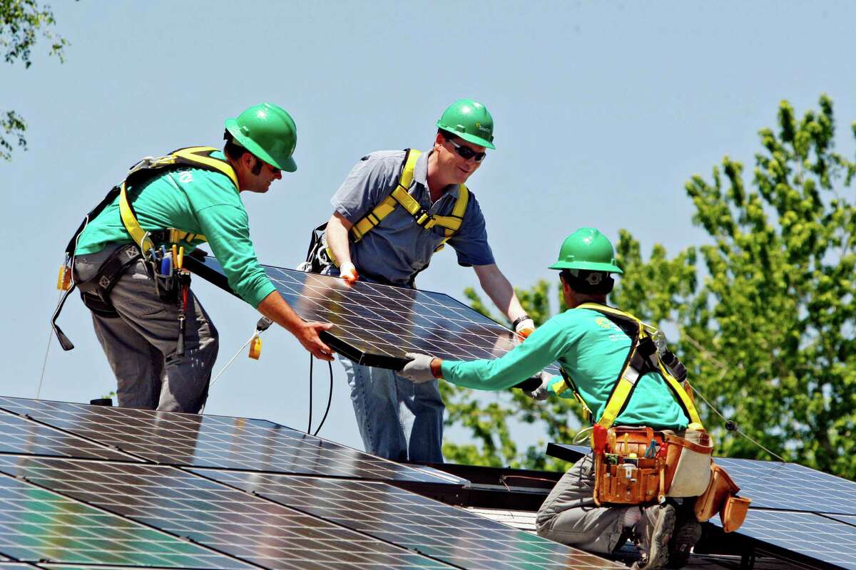 FILE - In this June 18, 2010, file photo, U.S. Senator Michael Bennet, D-Colo., center, helps as Solar City employees Jarret Esposito, left, and Jake Torwatzky, right, install a solar panel on a home in south Denver. The solar panel installer SolarCity said Wednesday, Jan. 15, 2014, it will launch an investment platform that will allow individuals and others to invest in rooftop solar systems directly with SolarCity. (AP Photo/Ed Andrieski, File)