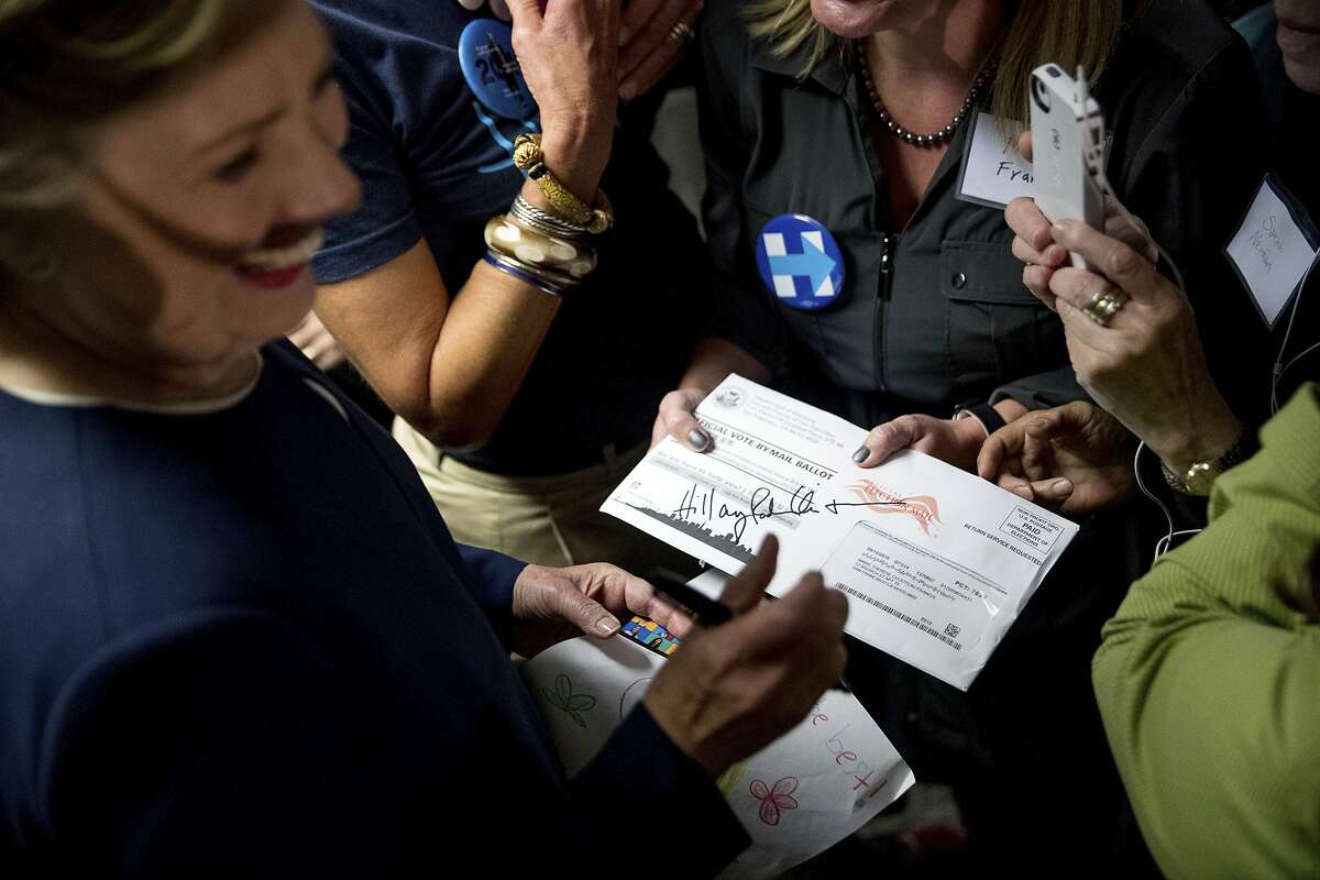 Democratic presidential candidate Hillary Clinton signs a vote-by-mail ballot letter as she greets volunteers at a campaign field office in San Francisco, Thursday, Oct. 13, 2016. (AP Photo/Andrew Harnik)