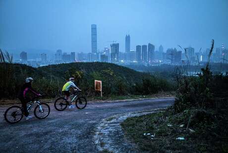 HONG KONG - APRIL 01:  People cycles at Kwu Tong with backdrop of Shenzhen on April 1, 2016 in Hong Kong. Despite recent protests seen from Hong Kong's opposition lawmakers on the construction of a high-speed rail linking the city to Shenzhen and Guangzhou, Hong Kong's future has been increasingly dependent on China's megacities across the border. Also known for being the global hub for China, Hong Kong's economic role in the region faces further challenges as its neighbouring mainland cities continue to grow. Last year the disappearance of a Hong Kong bookseller, followed by his reappearance on the mainland, has caused concerns that security officers from mainland China had taken him across the 37km-long border, which would have violated the "one country, two systems" arrangement since the return of Hong Kong on 1997.  (Photo by Lam Yik Fei/Getty Images)