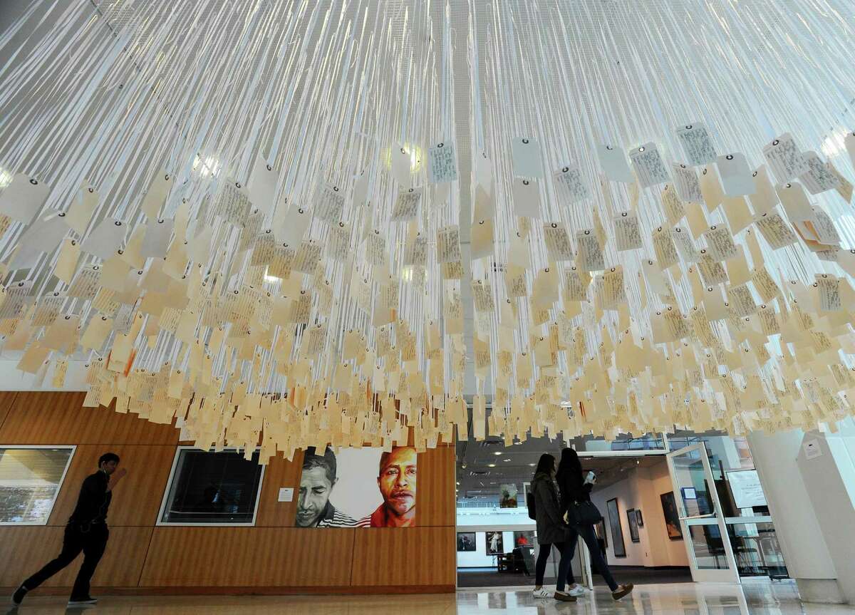 Students walk past the art installation "... and counting," created by Ann Lewis, inside the atrium of UConn-Stamford in Stamford, as part of the art exhibit "Race and Revolution." Lewis created an interactive installation that presents the facts around each police-related death in the United States in 2016, with each victim getting their own toe tag.
