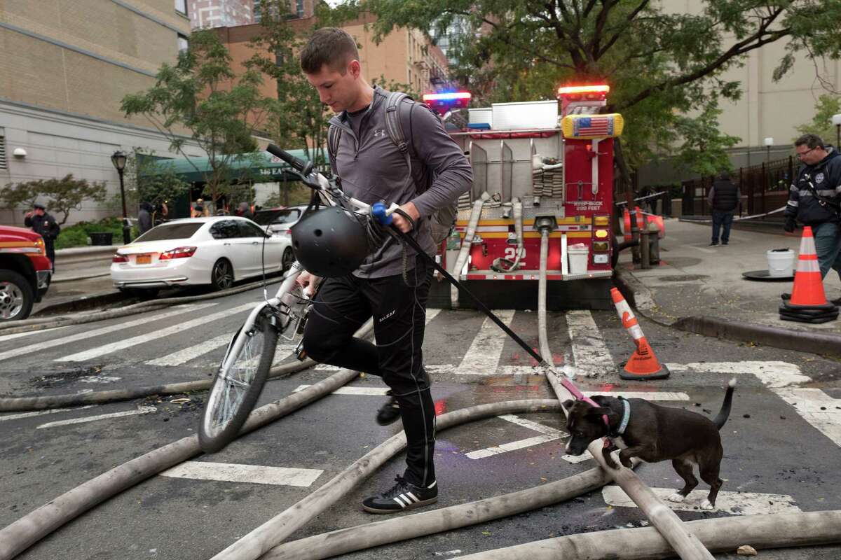 A bicyclist and his dog navigate firehoses on a Manhattan street following an early morning fire, Thursday, Oct. 27, 2016, in New York. The overnight blaze tore through an apartment building in Manhattan's Upper East Side. (AP Photo/Mark Lennihan) ORG XMIT: NYML102