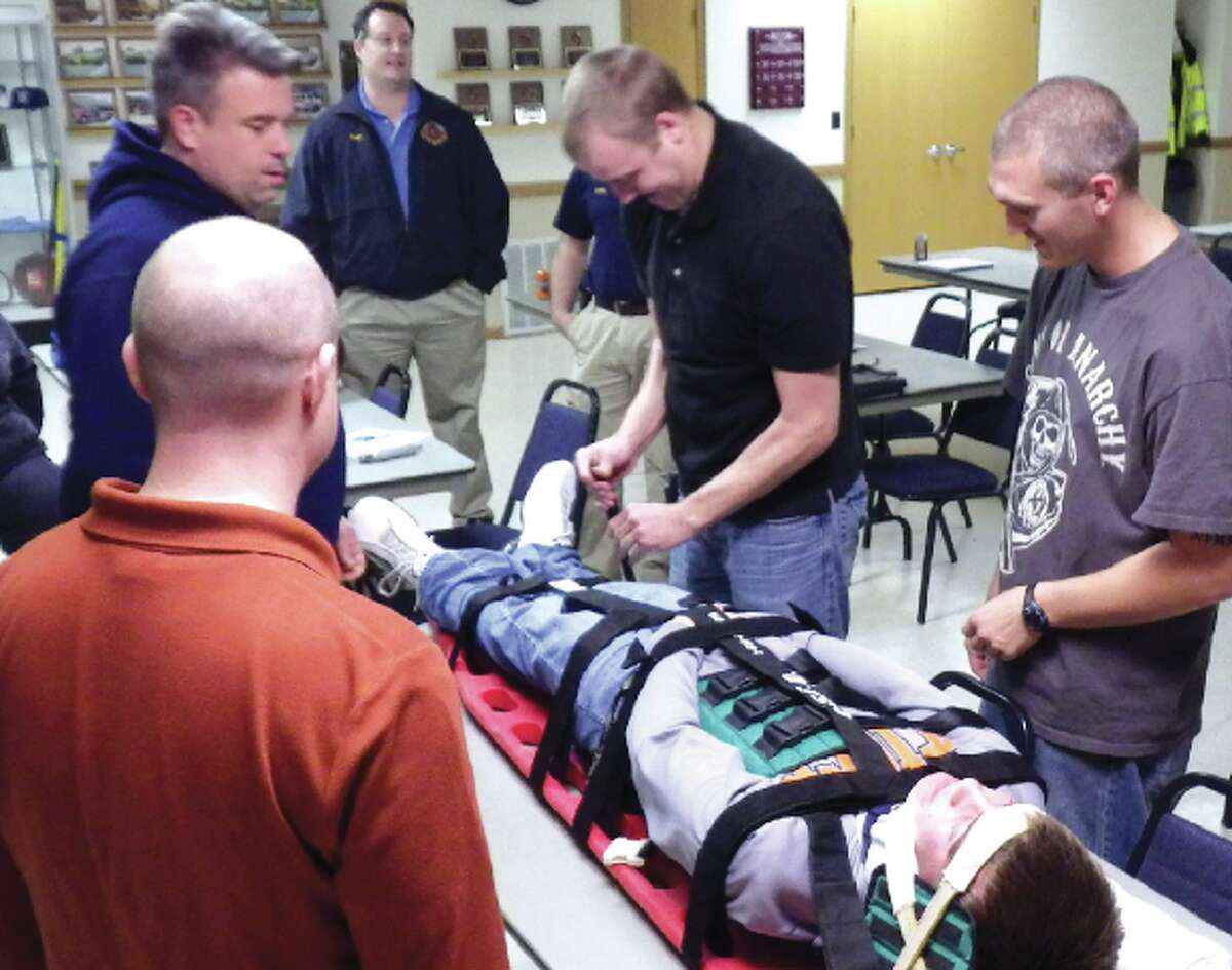 Holiday Shores Firefighters Mark Thornsberry (back to camera) Lt. Jim O’Brien, Doug Saye, Ryan Frank, Mike Thoe surround firefighter candidate Dakota Parish, who plays the victim during the International Trauma Life Support course recently conducted at the Holiday Shores firehouse. During the class members must practice “trauma packaging” using a Kendrick Extrication Device, velcro straps and a long backboard immobilizing the victim to reduce the chance of further injury while moving or transporting them.