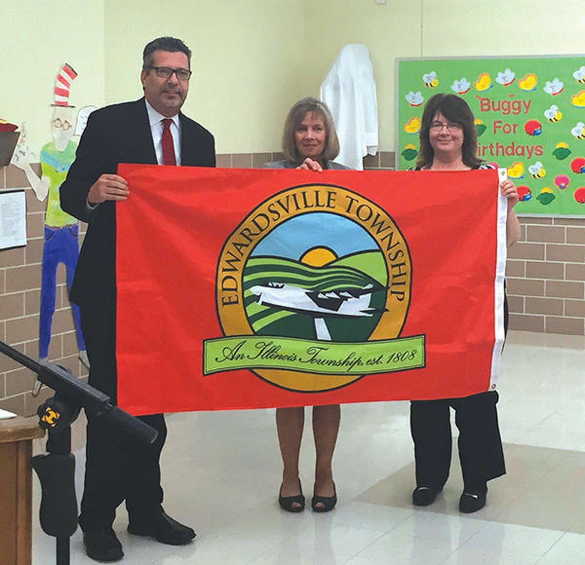 Edwardsville Township Supervisor Frank Miles, left, presents a township flag to Edwardsville District 7 Superintendent Lynda Andre, center, and Board of Education President Monica Laurent at Monday's meeting.