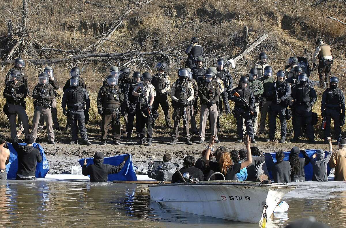 Dakota Access Pipeline protesters stand waist deep in the Cantapeta Creek, northeast of the Oceti Sakowin Camp, near Cannon Ball, N.D., Wednesday, Nov. 2, 2016. Officers in riot gear clashed again Wednesday with protesters near the Dakota Access pipeline, hitting dozens with pepper spray as they waded through waist-deep water in an attempt to reach property owned by the pipeline's developer. (Mike Mccleary/The Bismarck Tribune via AP)