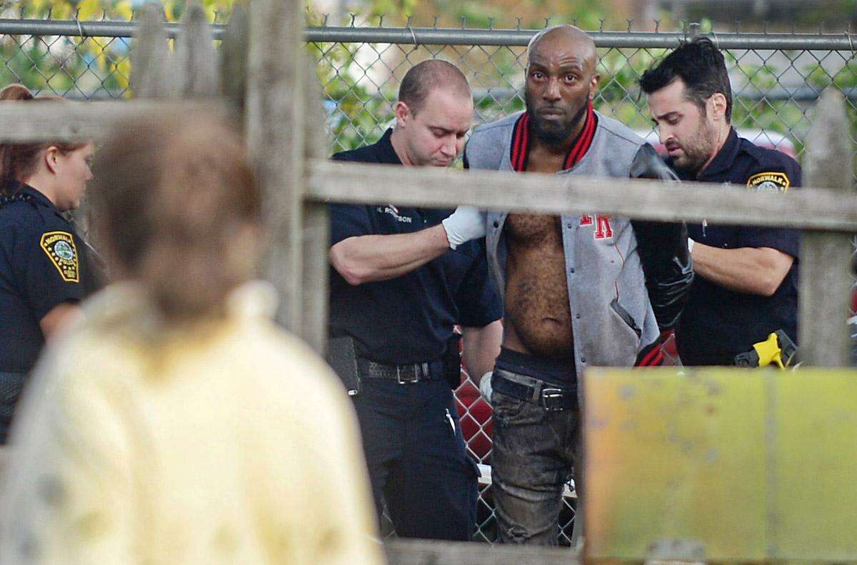 A neighbor looks on as Norwalk police apprehend a suspect on a reported narcotics offense in the yard of a Concord Street home Thursday. Dozens of officers responded to the scene around Columbus Magnet School and King Kennedy housing complex following a foot pursuit with officers.