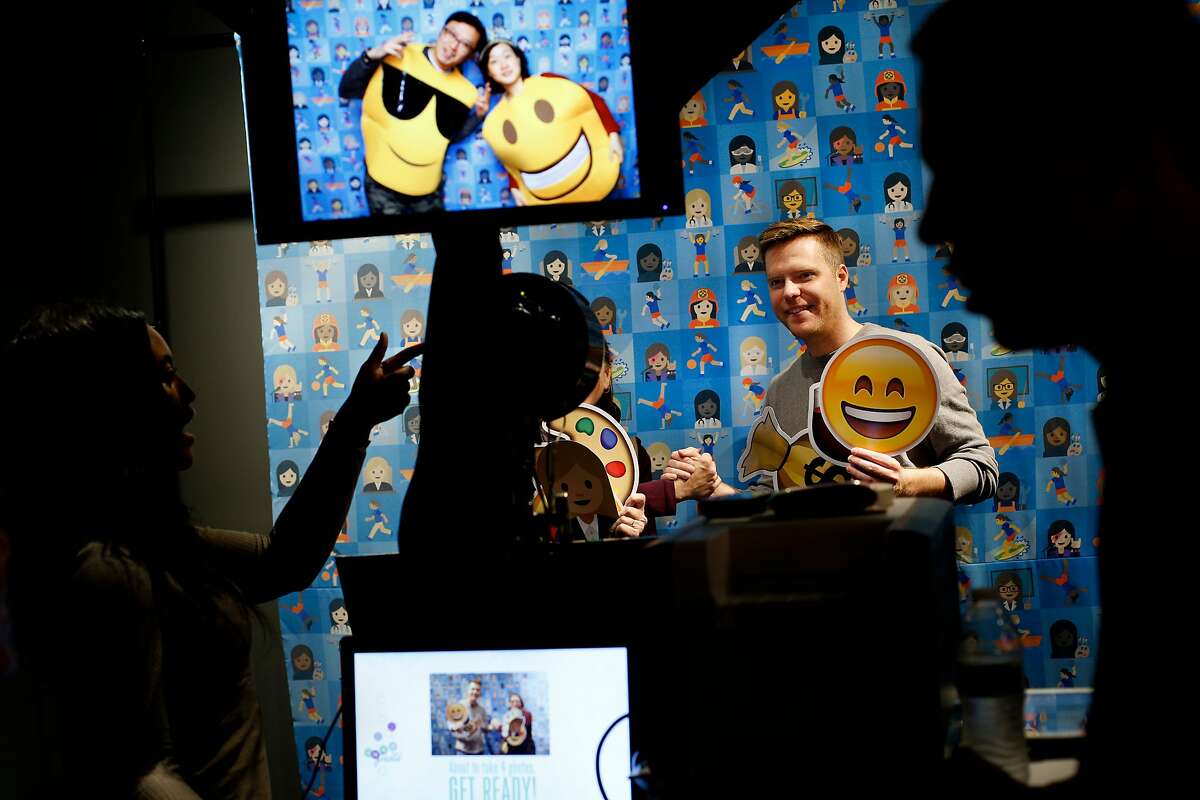 From left: Naomi Wardell takes a photo of Daniel Tate, who is holding a smiley-face emoji at the photobooth, during the first-ever Emojicon, at the Westfield San Francisco Centre, on Saturday, Nov. 5, 2016 in San Francisco, Calif.