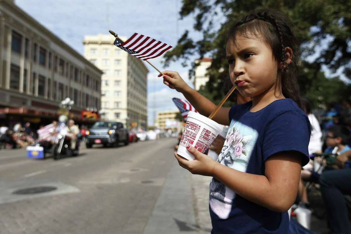 Divinity Muniz, 6, sips on a drink while waving her American flag during the annual Veteran's Day parade in downtown on Saturday, Nov. 12, 2016. Military veterans were honored with a parade through downtown San Antonio as parade watchers waved flags and said "thank you" aloud to active and retired military who took part in the parade. (Kin Man Hui/San Antonio Express-News)