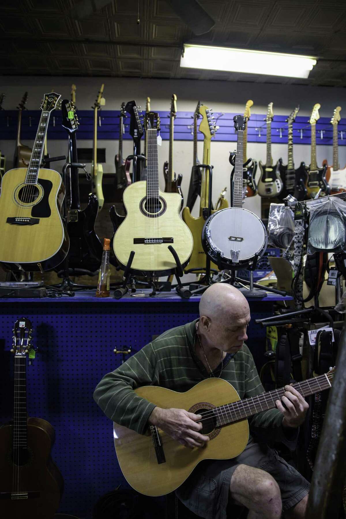 Alex Hussey, a regular customer, strums a guitar amid the vast selection at the Music Guild in Danbury.
