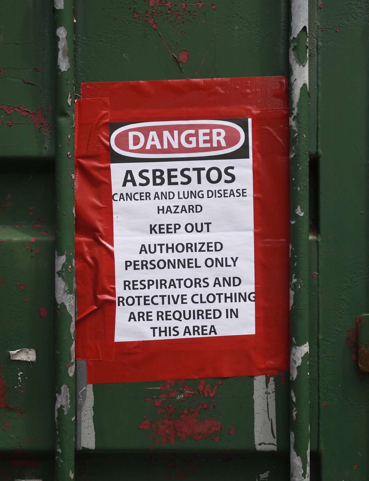 An asbestos warning sign hangs on a dumpster outside Julian Curtiss School in Greenwich, Conn. Monday, Aug. 3, 2015. The school is currently having asbestos removed from some of its classrooms.