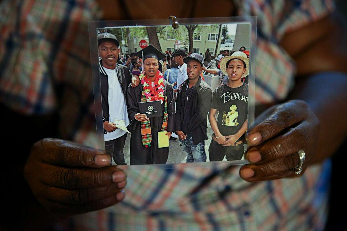 Teresa Jackson holds a photo of her son Roderick Travon Godfrey (second from left), family friend Deante Antonio Miller (right) on Tuesday, Nov. 29, 2016 in Oakland, Calif. Godfrey and Miller, both age 19, were both shot and killed on Monday at approximately 10:15 a.m. on the 700 block of 39th Street, between West Street and Martin Luther King Jr. Way, police said. No suspect was identified or arrested in the killings.