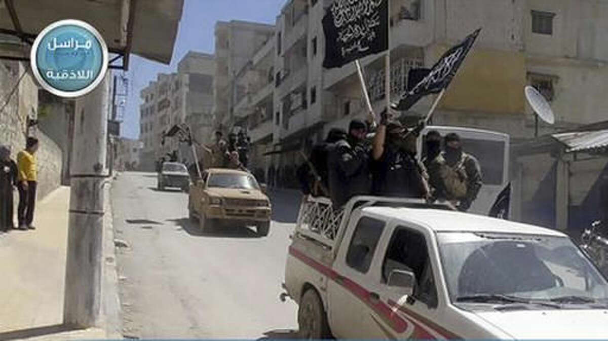 FILE - In this file photo posted on the Twitter page of Syria's al-Qaida-linked Nusra Front on April 25, 2015, which is consistent with AP reporting, Nusra Front fighters stand on their vehicles and wave their group's flags as they tour the streets of Jisr al-Shughour, Idlib province, Syria. The Syrian government has forced thousands of insurgents and their families to relocate to the northern Idlib province as part of truce deals, a move that rebels suspect is aimed at gathering them far from the capital where they can later be eliminated. The al-Qaida stronghold is now home to several insurgent groups, some with radical ideologies, and has been compared to Kandahar, the Taliban’s onetime seat of power in Afghanistan. (Al-Nusra Front Twitter page via AP, File)
