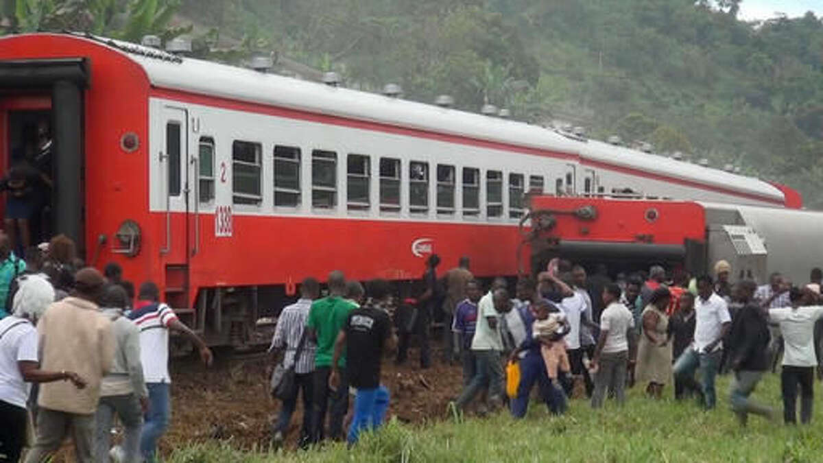In this image made from video, people walk beside a derailed train carriage after an accident in Eseka, Cameroon, Friday, Oct. 21, 2016. Cameroon's transport minister says at least 53 people have died after a train overloaded with passengers derailed along the route that links the country's two major cities. (Equinox TV via AP)