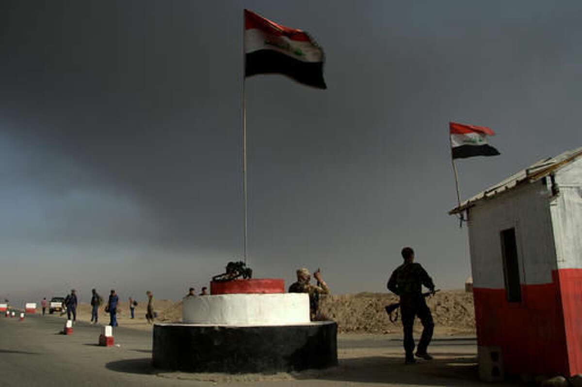 Iraqi troops guard a checkpoint near the village of Awsaja, Iraq, as smoke from fires lit by Islamic State militants at oil wells and a sulfur plant fills the air on Saturday, Oct. 22, 2016. U.S. military officials say that a fire at the sulfur plant in northern Iraq is creating a potential breathing hazard for American forces and other troops at a logistical base south of Mosul. (AP Photo/Adam Schreck)