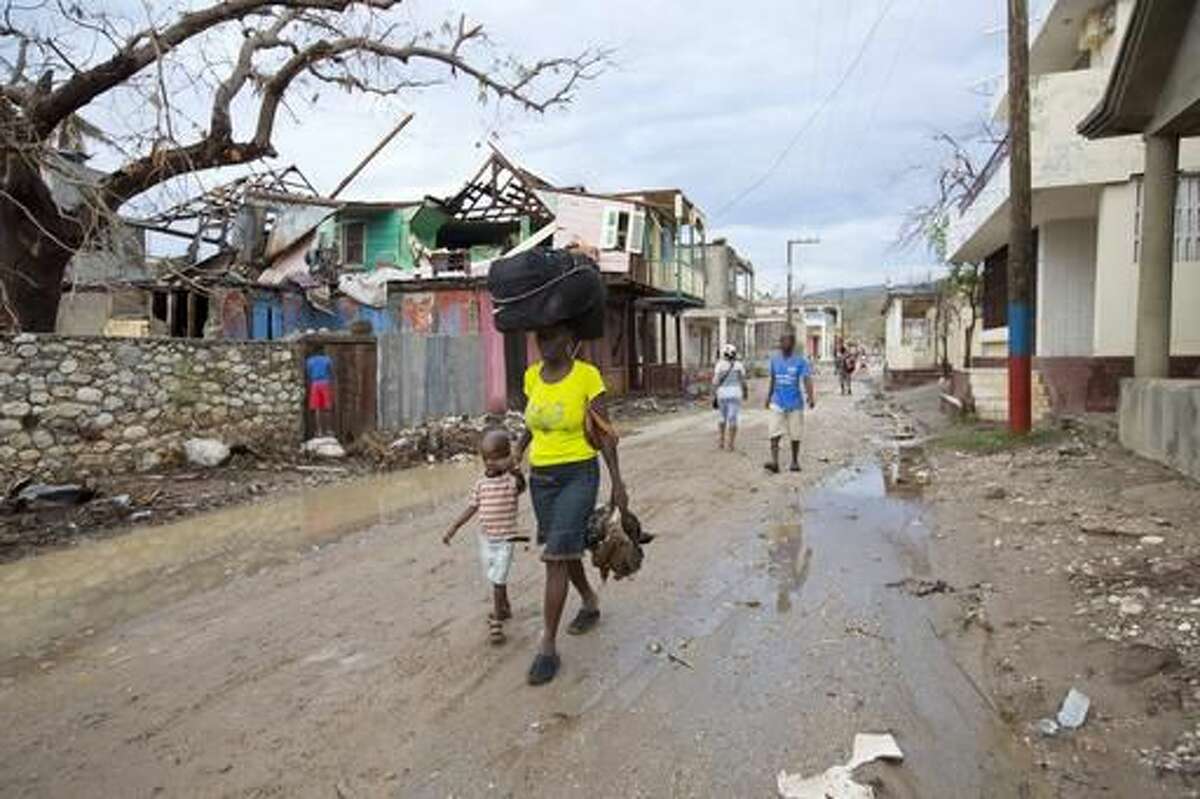 In this Tuesday, Oct. 18, 2016 photo, a mother and her child walk to a nearby bus stop with their personal belongings, in Port-a-Piment, a district of Les Cayes, Haiti, where they will board a bus to the capital to stay with relatives, because Hurricane Matthew destroyed their home. Government personnel and an army of international aid workers are delivering more relief supplies to people, but local authorities say it is falling well short of meeting desperate needs. (AP Photo/Dieu Nalio Chery)
