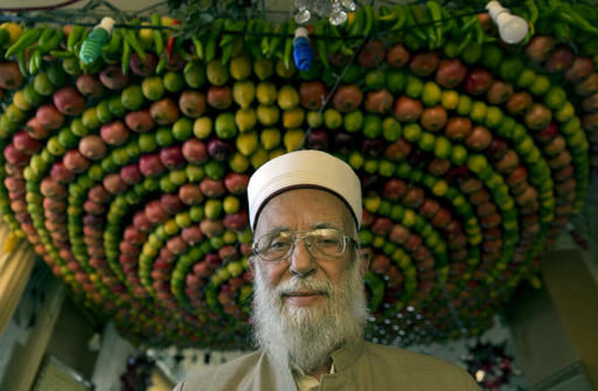 In this Sunday, Oct. 16, 2016 photo, the high priest of the ancient Samaritan community Abdullah Wasef Tawfiq poses for a photo inside his house, during their celebrations of the week-long biblical holiday of Sukkot, or Feast of Tabernacles, on Mount Gerizim, overlooking the West Bank city of Nablus. In the Bible, God commands the people of Israel to build huts symbolizing the Israelites’ encampments as they wandered the desert following the exodus from Egypt. Unlike the outdoor huts Jews construct on the holiday, Samaritans build exquisite canopies of densely packed fruit, which are attached to metal frames and perched on stilts or suspended from living room ceilings. (AP Photo/Nasser Nasser)