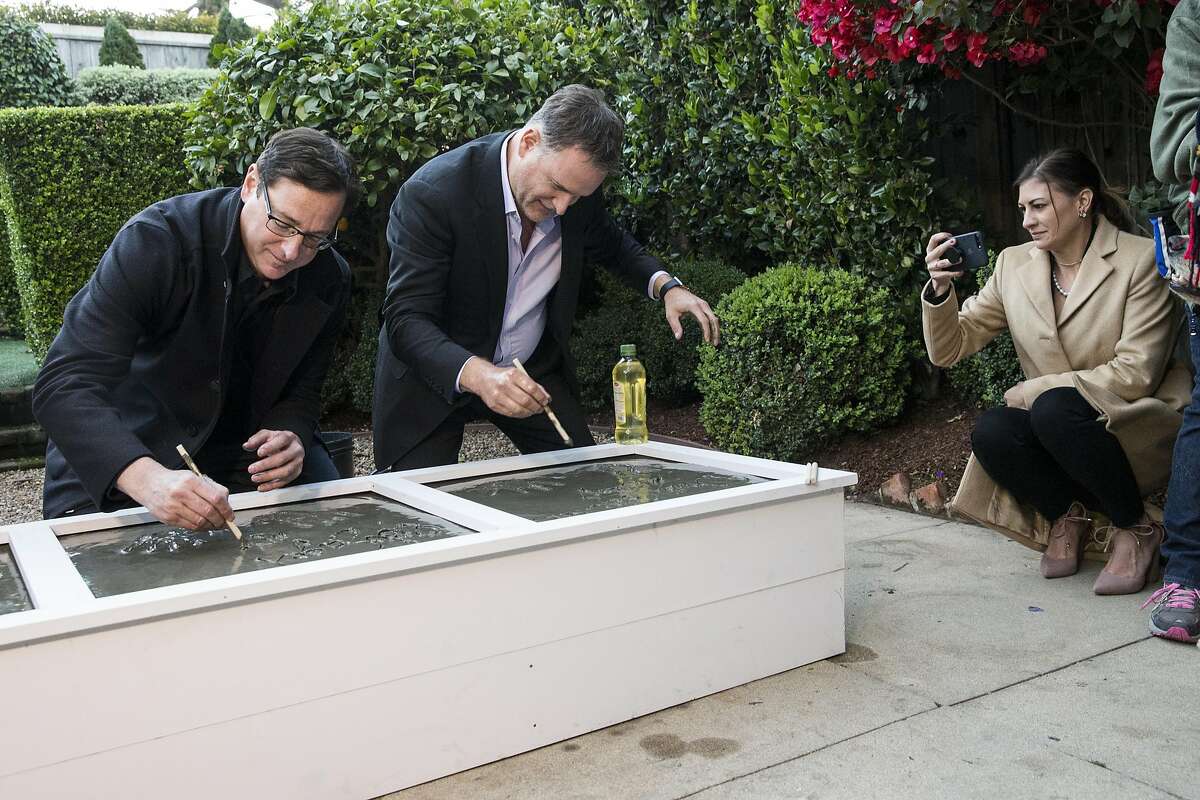 "Full House" cast members Bob Saget and Dave Coulier write their names in cement as Coulier's wife Melissa Coulier (left to right) snaps a photo in the backyard of the property used in the sitcom as the home of the fictional Tanner family during press event for the second season of the Netflix sequel "Fuller House" in San Francisco, Calif., on Friday, December 2, 2016. "Full House" creator Jeff Franklin recently purchased the property.