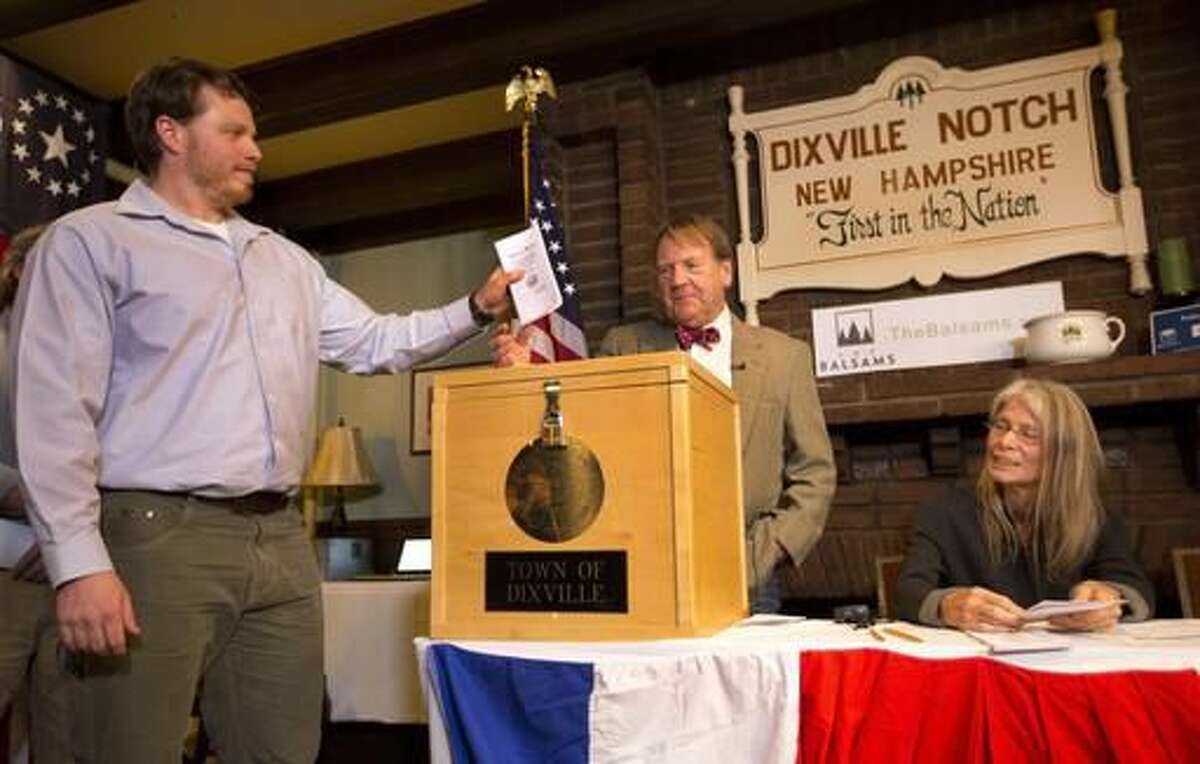 CORRECTS TO DIXVILLE NOTCH FROM DIXVILLE NOTCHE AND CLARIFIES VOTES- Dixville Notch's first voter Clay Smith drops his ballot into the box as moderator Tom Tillotson watches Tuesday, Nov. 8, 2016, in Dixville Notch, N.H. Dixville Notch, where the nation's first voters cast their ballots on Election Day, had Democratic presidential candidate Hillary Clinton beating Republican Donald Trump. (AP Photo/Jim Cole)