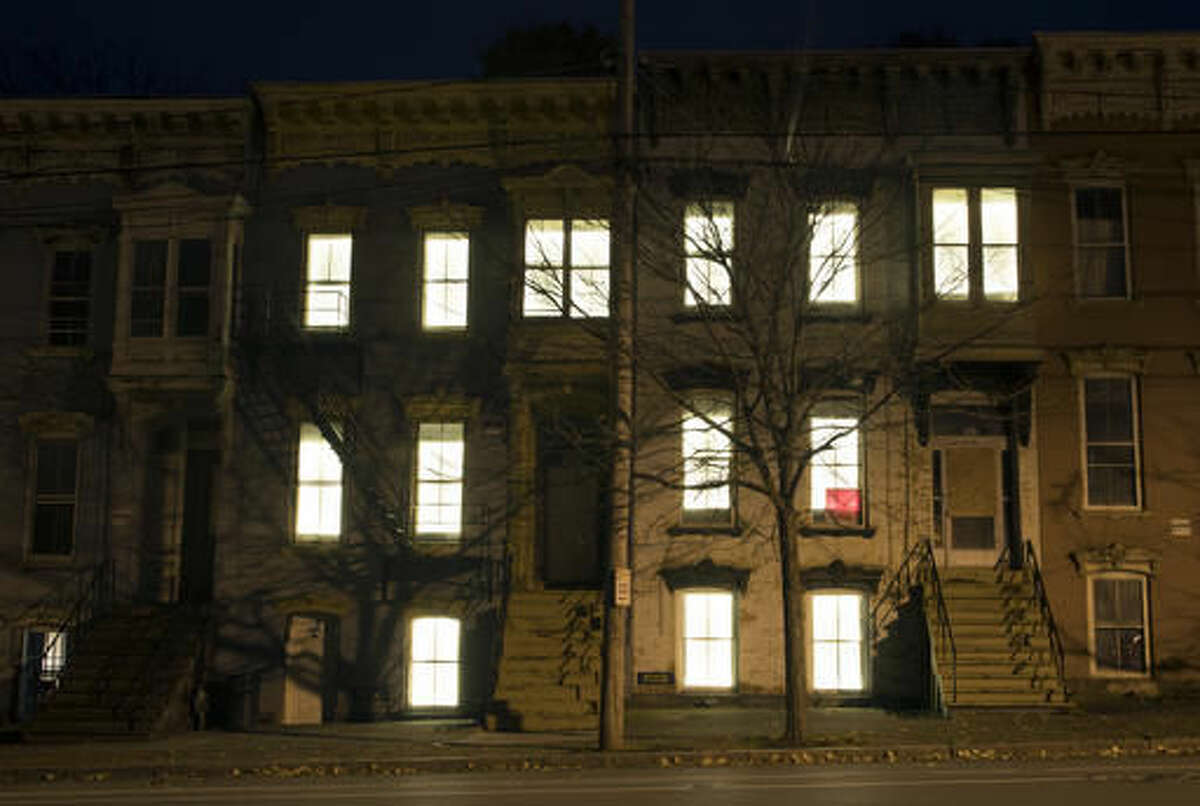 In this Friday, Oct. 28, 2016 photo, windows in vacant buildings are illuminated with LED lights in Albany, N.Y. Windows in more than 150 abandoned buildings in three upstate New York cities have been fitted with light-emitting diodes that steadily brighten and fade, giving the effect of slow breathing. The two-month public art project provides something pretty for gritty neighborhoods of Albany, Schenectady and Troy. (AP Photo/Mike Groll)