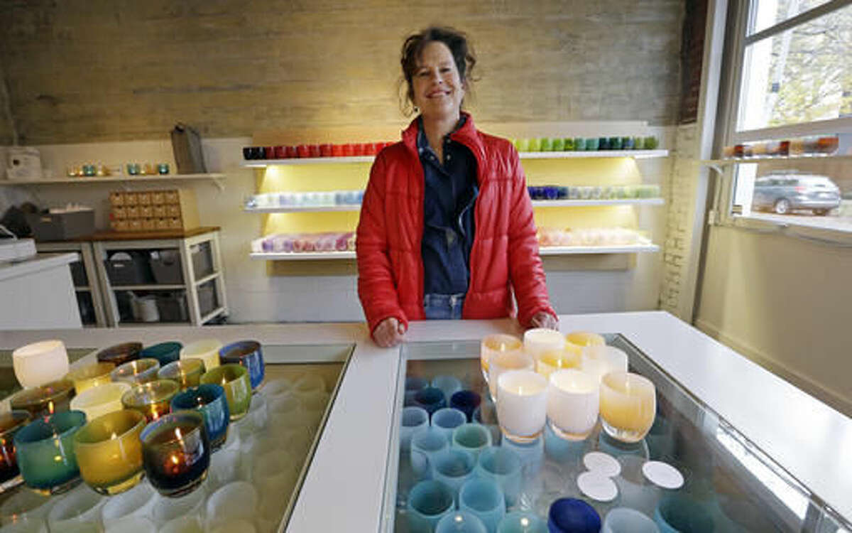 In this Tuesday, Nov. 22, 2016, photo, Lee Rhodes, owner of Glassybaby, poses for a photo near votive candle holders on display at her shop in Seattle. Rhodes says that she has seen her products with positive labels such as "kindness," "comfort" and "hope," surge past holiday themes like "elf" and "joy" since Election Day. (AP Photo/Elaine Thompson)
