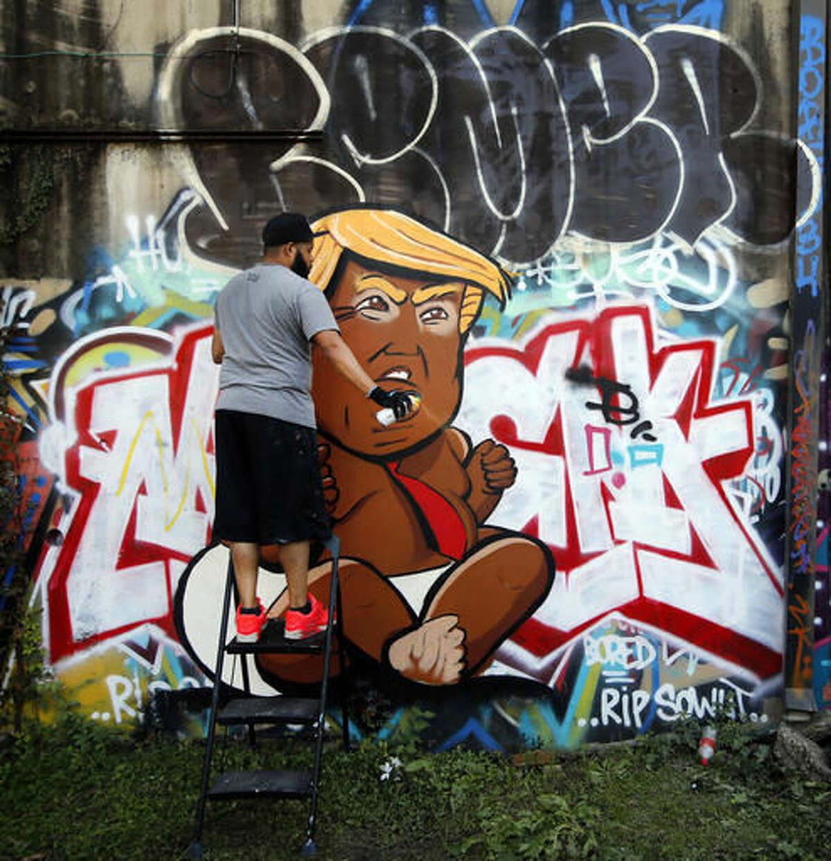 In a Saturday, Nov. 12, 2016 photo, Dallas artist Jeremy Biggers clears his spray can as he paints a caricature of President-elect Donald Trump during GO PAINT DAY at the Fabrication Yard in Dallas. This is only the third time the realism painter has created artwork with a spray can. The two days are dedicated to celebrating hip hop history month with paint, music, dancing and community. (Tom Fox/The Dallas Morning News via AP)