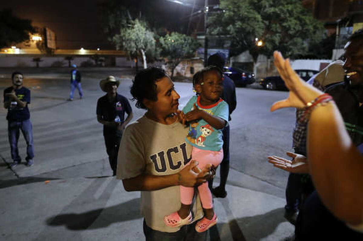 FILE - In this Nov. 14, 2016 file photo, Guatamalan Elvin Vazquez, center, holds a Haitian girl migrating with her family, at a migrant shelter in Tijuana, Mexico. A surge in border crossings and a lack of immigration jail space have prompted the federal government to start releasing Haitian immigrants who have been entering the country in large numbers in recent months, backtracking on a pledge to jail the migrants. A U.S. government official said the decision to free Haitians arriving in Arizona and California is in response to a lack of jail space. Thousands of Haitians have arrived at the U.S. border with Mexico in recent months, many after traveling 7,000 miles by foot, taxi and bus. (AP Photo/Gregory Bull, File)