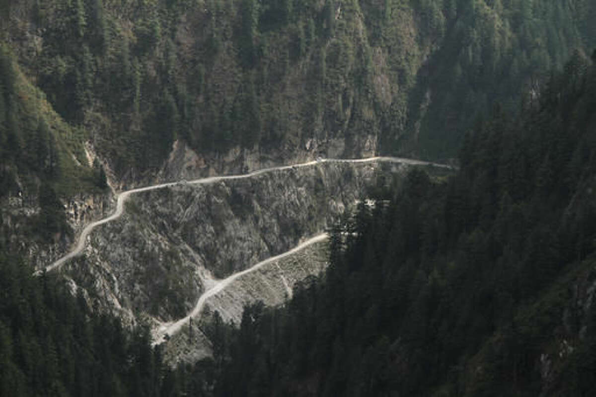 In this Tuesday Oct. 4, 2016 photo, cars move on the narrow shabby road cut along the steep slope near Malana village in the northern Indian state of Himachal Pradesh. Nestled deep in the higher reaches of the Indian Himalayas, Malana has become one of the world's top stoner destinations, and a symbolical battleground for India's fight against 'charas,' the black and sticky hashish that has made the village famous. (AP Photo/Rishabh R. Jain)