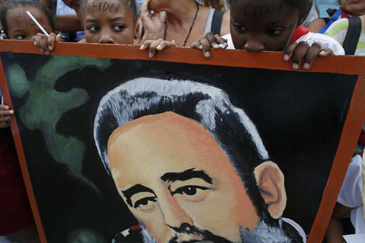 Children stand behind a portrait of the late cuban leader Fidel Castro as they wait for the arrival of the motorcade carrying the ashes of Castro at the Cespedes park in Santiago, Cuba, Saturday, Dec. 3, 2016. After days of national mourning in Cuba and a tour of his ashes through the countryside, his remains have arrived to the city where they will be laid to rest.(AP Photo/Dario Lopez-Mills)