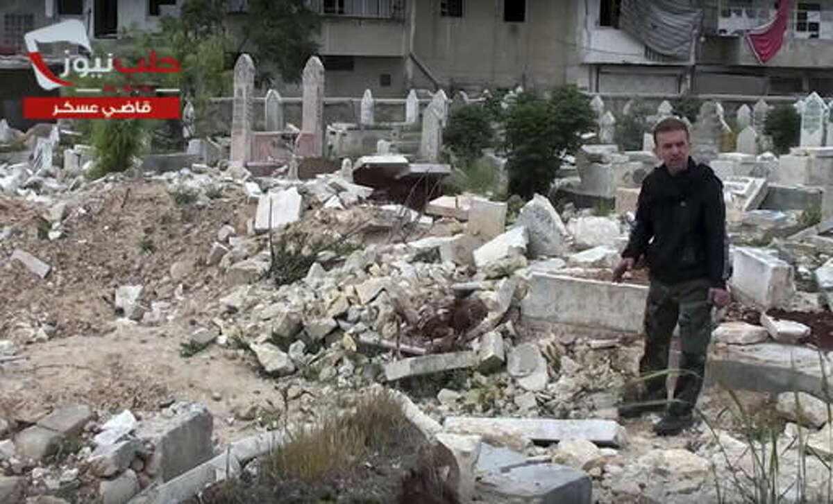 This frame grab from video provided on April. 19, 2014 by the Aleppo News Network, shows a man pointing to the aftermath of bombings of a cemetery in eastern Aleppo city, Syria. The old Aleppo cemetery filled up a year ago, the new one filled up this week, and now the dead are left in the besieged enclave's streets, buried in backyards and overwhelming the morgues. Dignity in death has been lost as the rebel-held enclave of eastern Aleppo that held out for four years collapses. (Aleppo News Network, via AP)