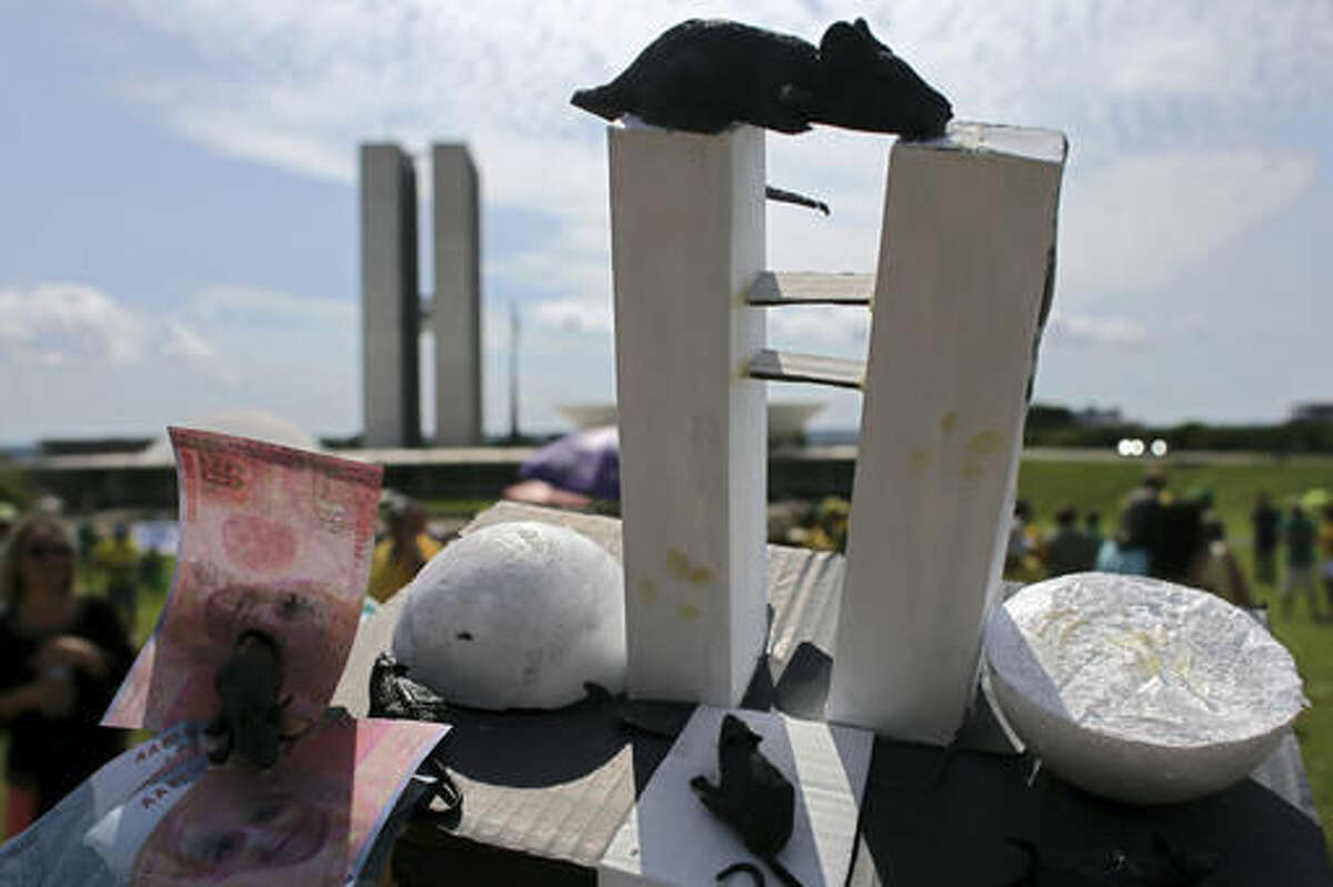 A demonstrator shows a replica of the building of the Brazilian National Congress with mice and money during a protest against corruption outside the National Congress, in Brasilia, Brazil, Sunday, Dec. 4, 2016. An investigation into a kickback scheme at the national oil company has shocked Brazilians both for the scale of corruption it has revealed and for the commitment of the judiciary to see it through in a country where many feel the powerful act with impunity. (AP Photo/Eraldo Peres)
