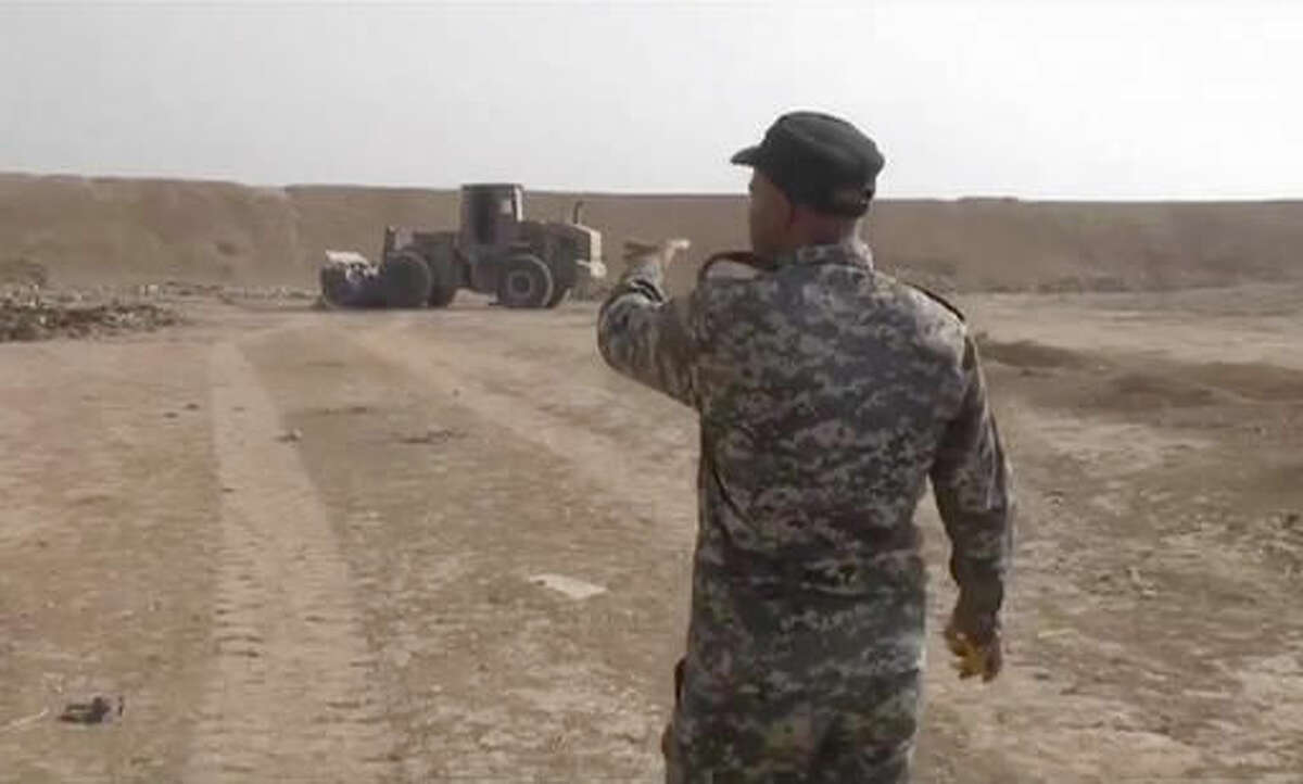In this Monday, Nov. 7, 2016 frame grab from video, an Iraqi federal police officer walks towards a mass grave in Hamam al-Alil, Iraq. The Iraqi military says it has found some 100 decapitated bodies in a mass grave south of the Islamic State-held city of Mosul. According to the spokesman for the Joint Military Command, Brigadier General Yahya Rasool, the bodies were discovered on Monday near the agricultural college in the town of Hamam al-Alil. (AP Photo)
