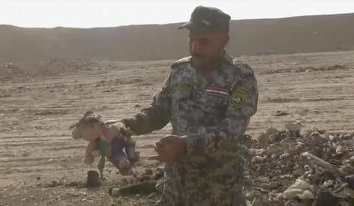 In this Monday, Nov. 7, 2016 frame grab from video, an Iraqi federal police officer holds a stuffed toy at the site of a mass grave in Hamam al-Alil, Iraq. Investigators are probing the mass grave that was discovered the previous day by troops advancing further into Islamic State-held territory near the city of Mosul. Associated Press footage from the site shows bones and decomposed bodies among scraps of clothing and plastic bags dug out of the ground by a bulldozer after Iraqi troops noticed the strong smell while advancing into the town of Hamam al-Alil. (AP Photo)