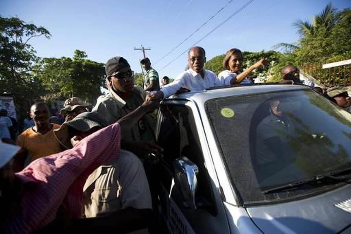 In this Wednesday, Nov. 16, 2016 photo, Haiti's former President Jean-Bertrand Aristide reaches out to shake a supporter's hand as he campaigns for presidential candidate Maryse Narcisse, riding alongside him in Arcahaie, Haiti. The electoral cycle began more than a year ago, but it’s been repeatedly derailed. A first-round presidential vote held in October 2015 was annulled due to complaints of fraud. ( AP Photo/Dieu Nalio Chery)
