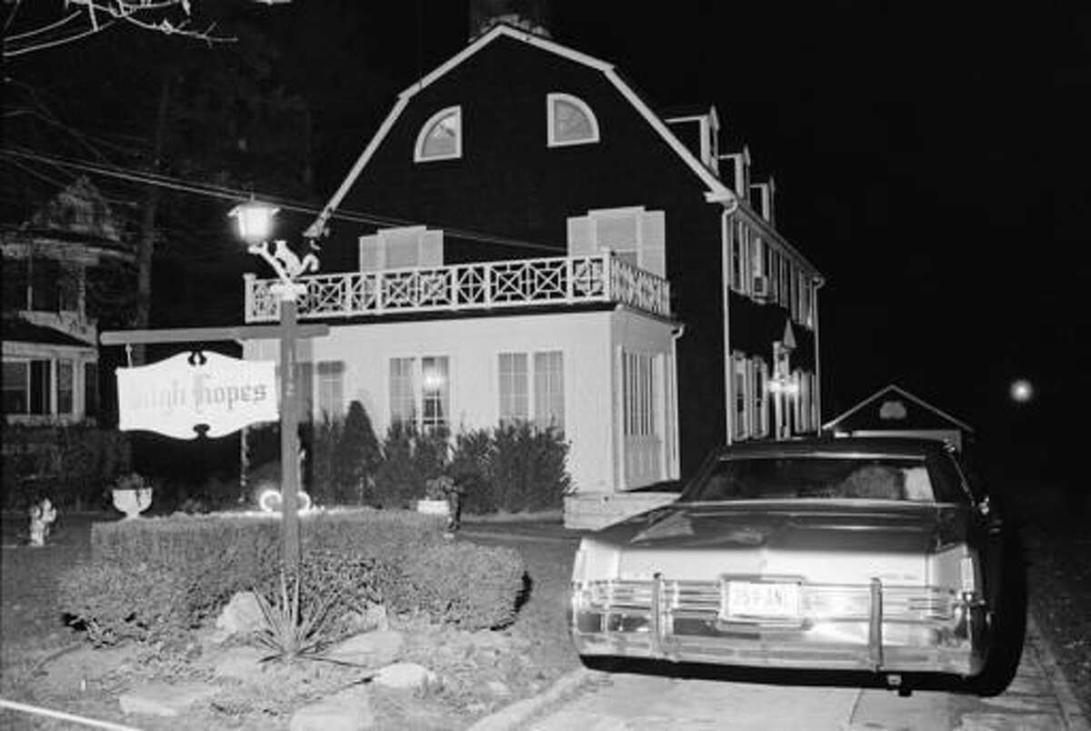 FILE - In this Nov. 14, 1974 file photo, police and members of the Suffolk County Coroner's Office investigate the murder of six people found shot in Amityville, N.Y. The Long Island home that served as the inspiration for the book "The Amityville Horror" and the subsequent films of the same name is being bought. Newsday reports, Friday, Nov. 18, 2016, the infamous 1927 Dutch Colonial went into contract this week. (AP Photo/Richard Drew, File)