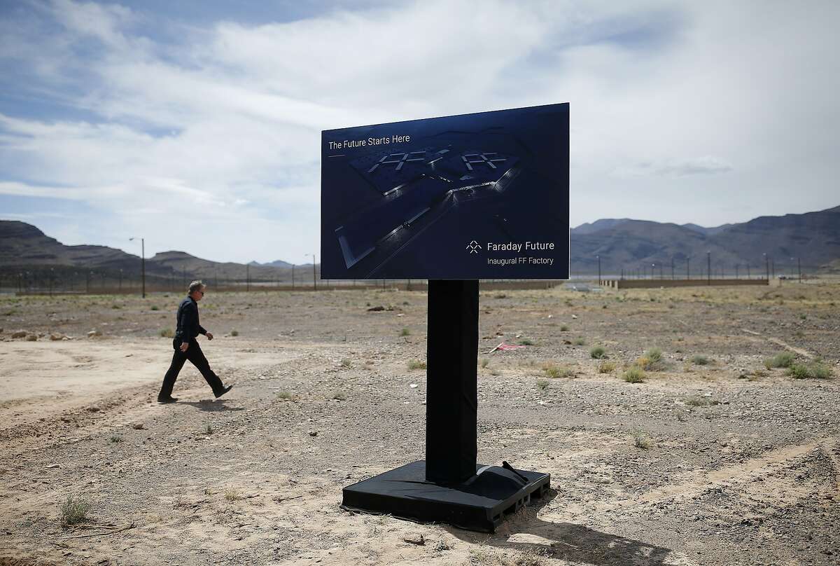 FILE - In this April 13, 2016, file photo, a man walks by a sign at an event to mark the start of construction for Faraday Future in North Las Vegas, Nev. Work has stopped at the site outside Las Vegas where upstart electric car company Faraday Future has said it plans to have vehicles that are still in the design phase rolling off a new $1 billion assembly line in 2018. Faraday Future spokesman Ezekiel Wheeler said Tuesday, Nov. 15, 2016, the pause after millions of dollars' worth of ground work at the Apex Industrial Park site will let the company put money and attention toward developing the concept car it wants to present at the big Consumer Electronics Show in Las Vegas in January. (AP Photo/John Locher, File)