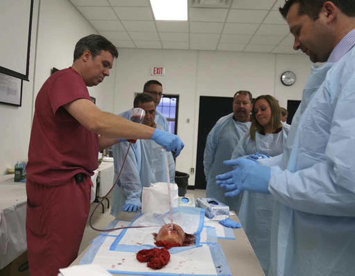 Dr. James Vosswinkel, left, the chief of trauma, emergency surgery, and surgical critical care, at Stony Brook University Hospital, demonstrates how to pack a gunshot wound on a fake body part during a first aid training session at Stony Brook University in New York, Tuesday, Nov. 29, 2016. A new federal initiative seeks to prevent deaths in terror attacks and school shootings by training ordinary people from custodians to administrators on how to treat gunshots, gashes and other injuries. Stony Brook doctors have reached out to local schools to offer the training, but are looking to expand the program as part of a federal Department of Homeland Security initiative to other schools, colleges and police departments across the country. (AP Photo/Michael Balsamo)