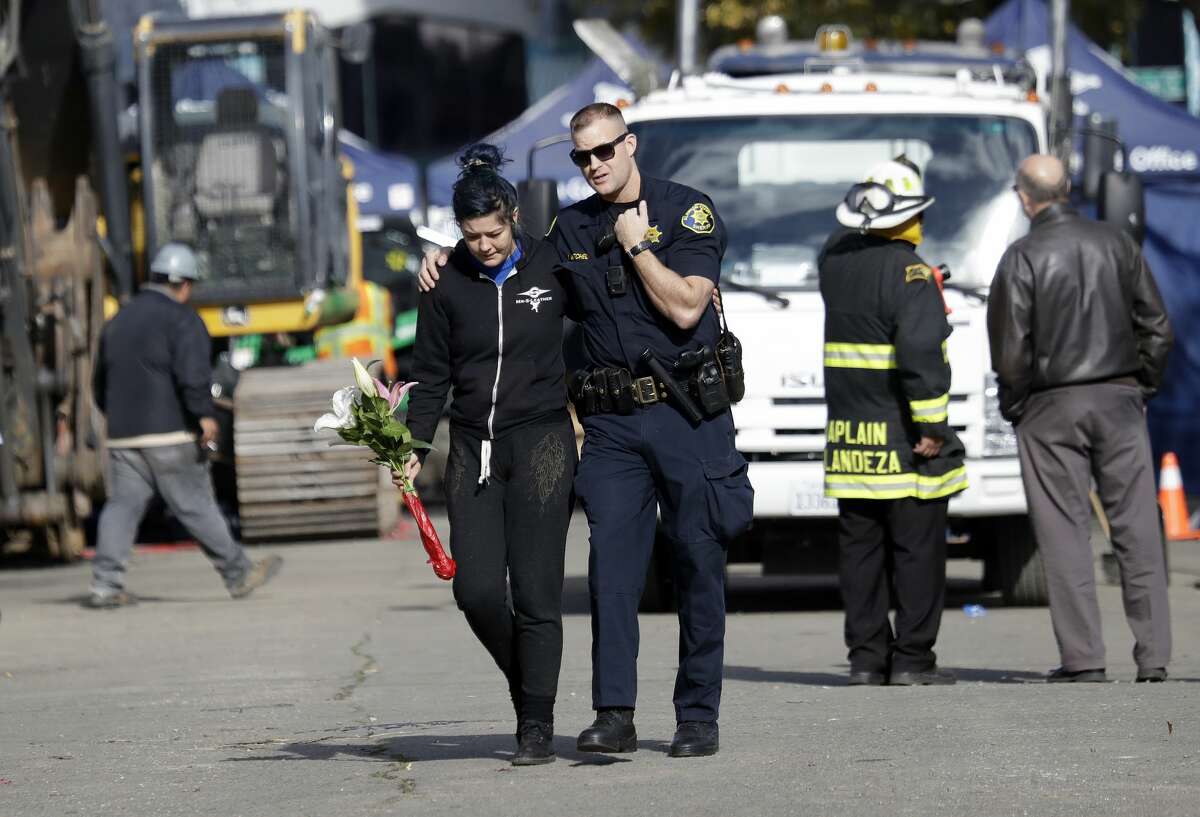 An Alameda County Sheriff, center, escorts a woman carrying flowers at the site of a warehouse fire Tuesday, Dec. 6, 2016, in Oakland, Calif. (AP Photo/Marcio Jose Sanchez)