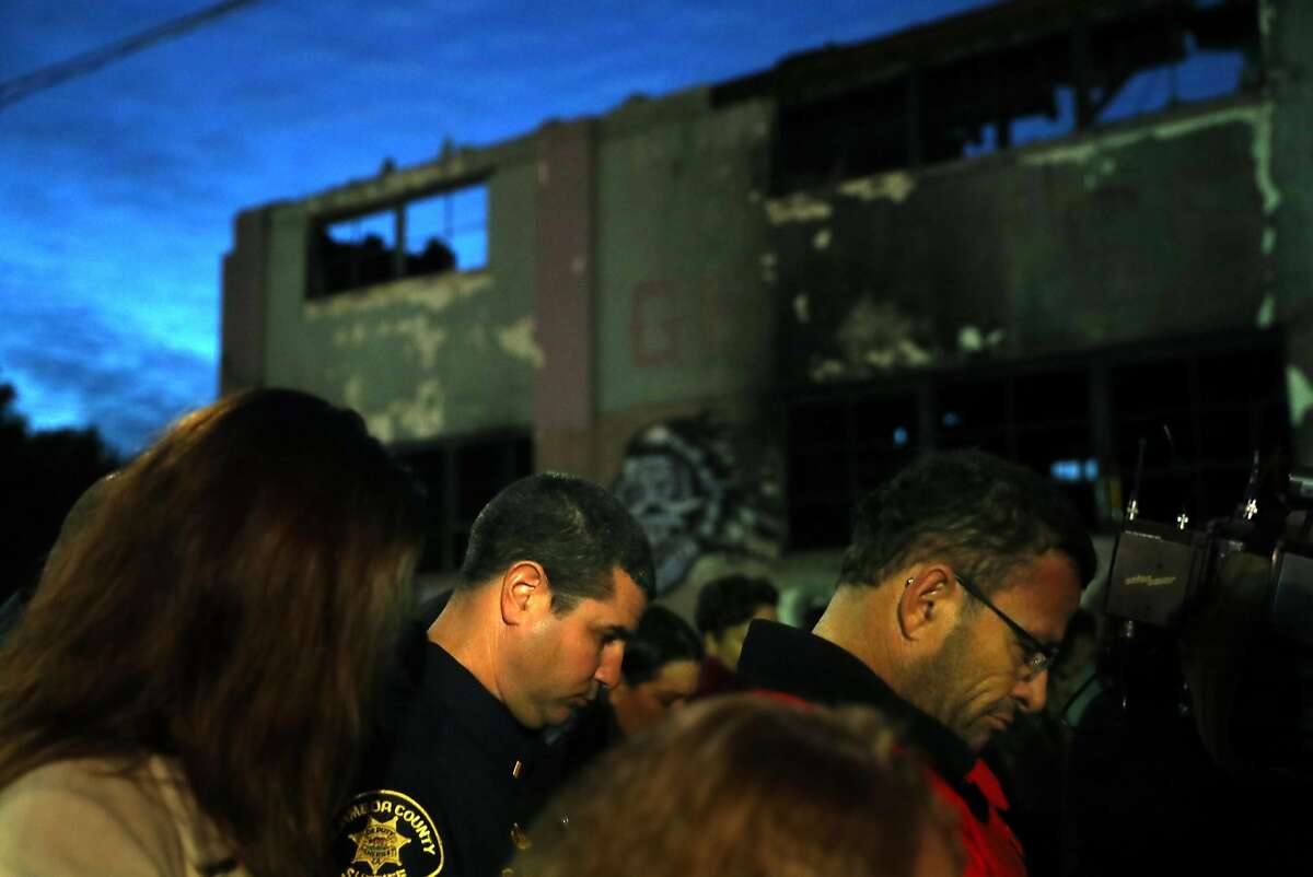 Attendees observe a moment of silence during a memorial service for the Ghost Ship warehouse fire victims in front of the structure on 31st Avenue in Oakland, Calif., on Monday, December 12, 2016.