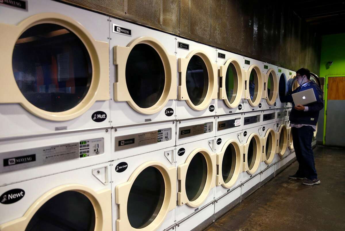 A customer removes clean laundry from a dryer at the Brainwash cafe and laundromat in San Francisco, Calif. on Friday, Dec. 16, 2016. Owner Jeff Zalles has noticed a dramatic drop in business ever since a large residential development currently under construction broke ground next door to the Brainwash and is concerned he may have to shut down.